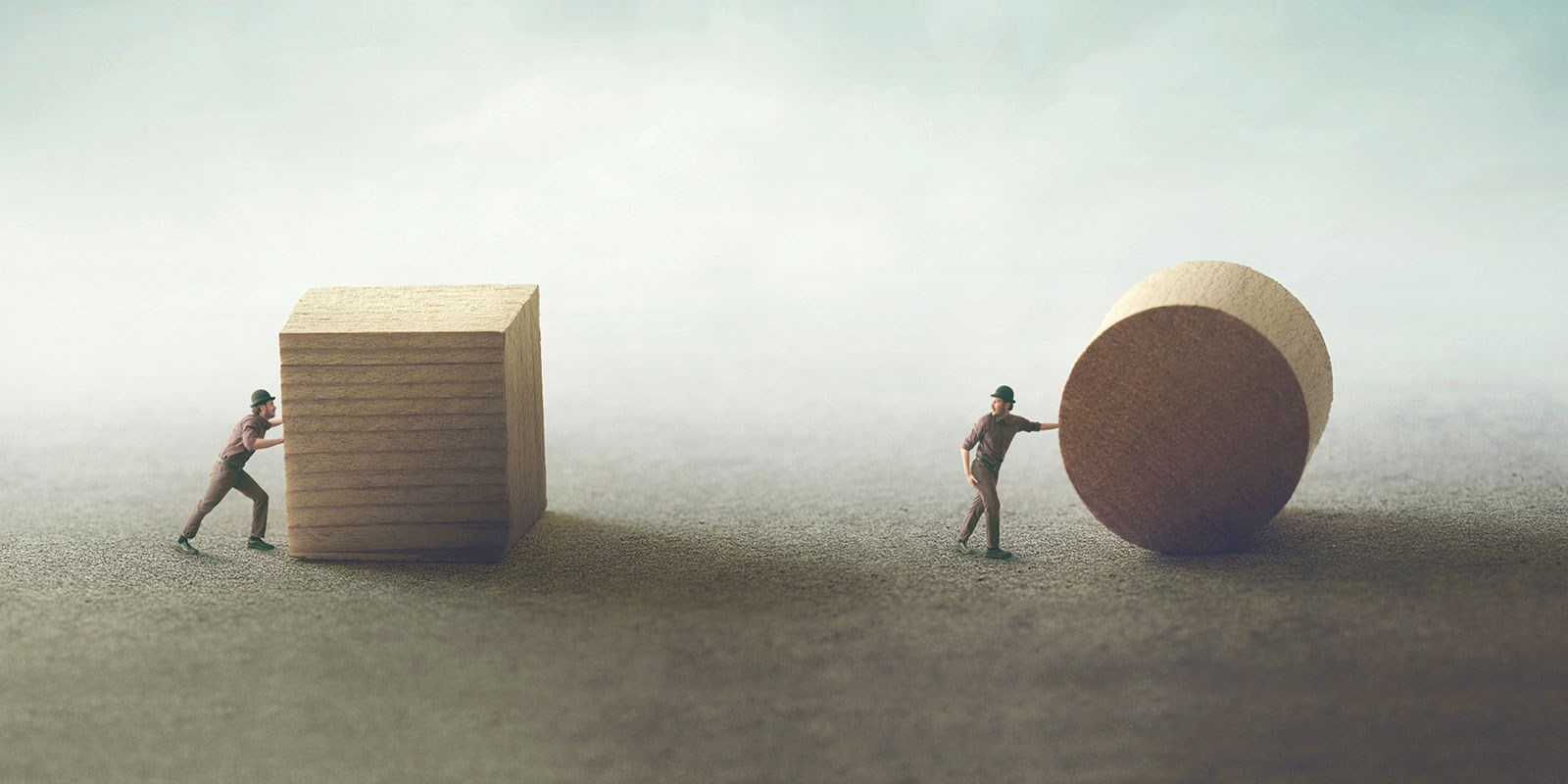 two men, one struggling to push a wooden cube, one easily pushing a wooden sphere