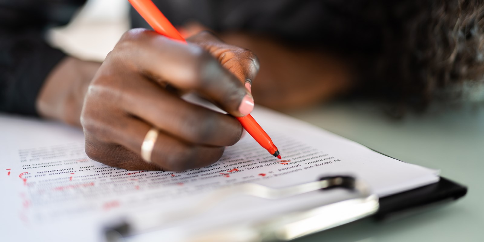 close up of hand holding red pen, marking up printed words