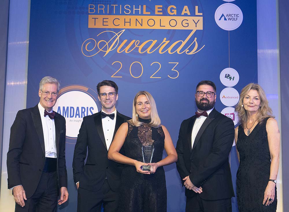 A group of people smiling, surrounding woman holding trophy for British Legal Technology award