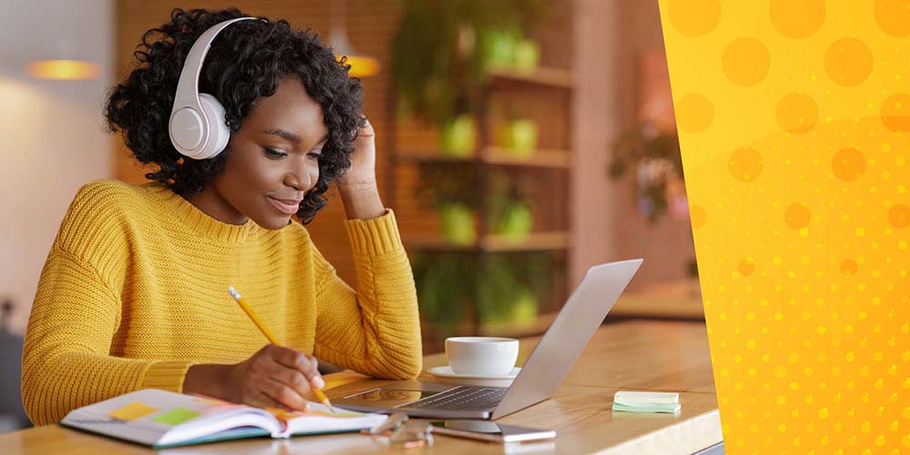 Black woman in yellow sweater with headphones taking notes