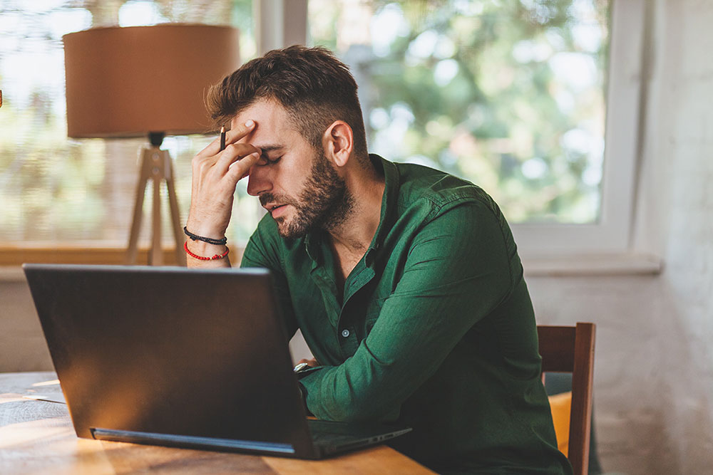 frustrated man using laptop with head in his hand